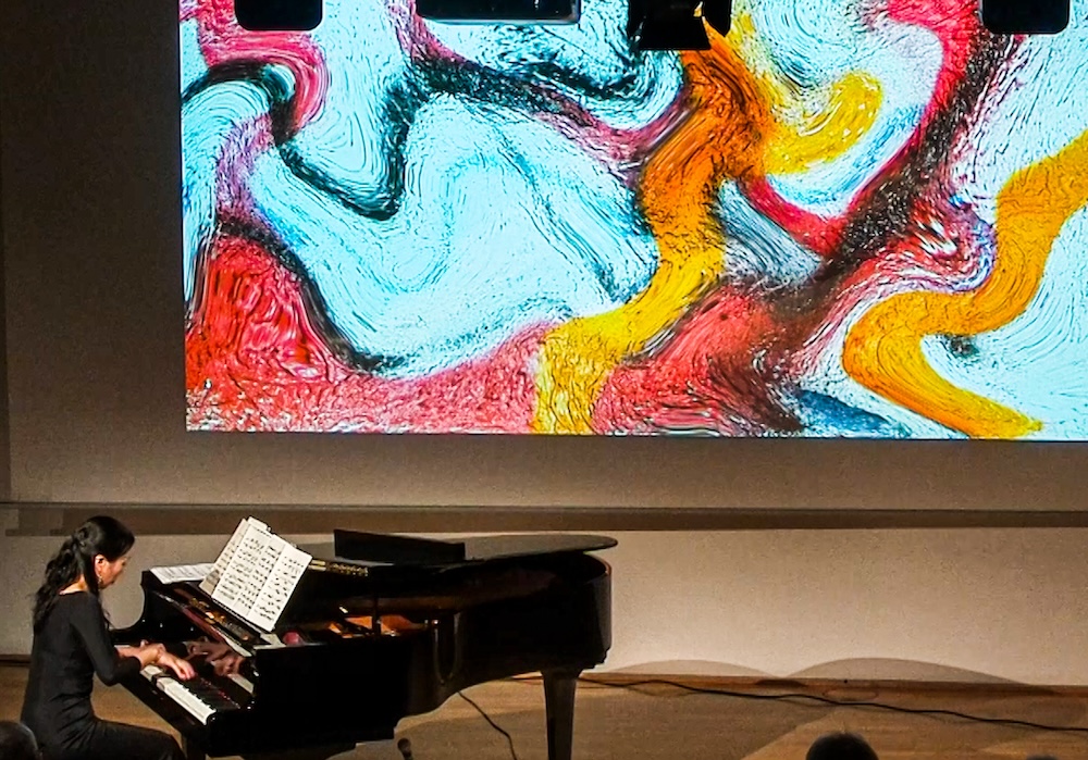 eine Pianistin am Konzertflügel, im Hintergrund ein abstraktes Bild